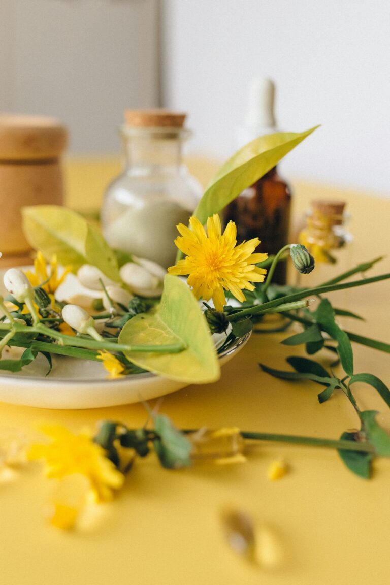 Close-up of herbal remedies featuring fresh flowers and essential oils on a yellow surface.